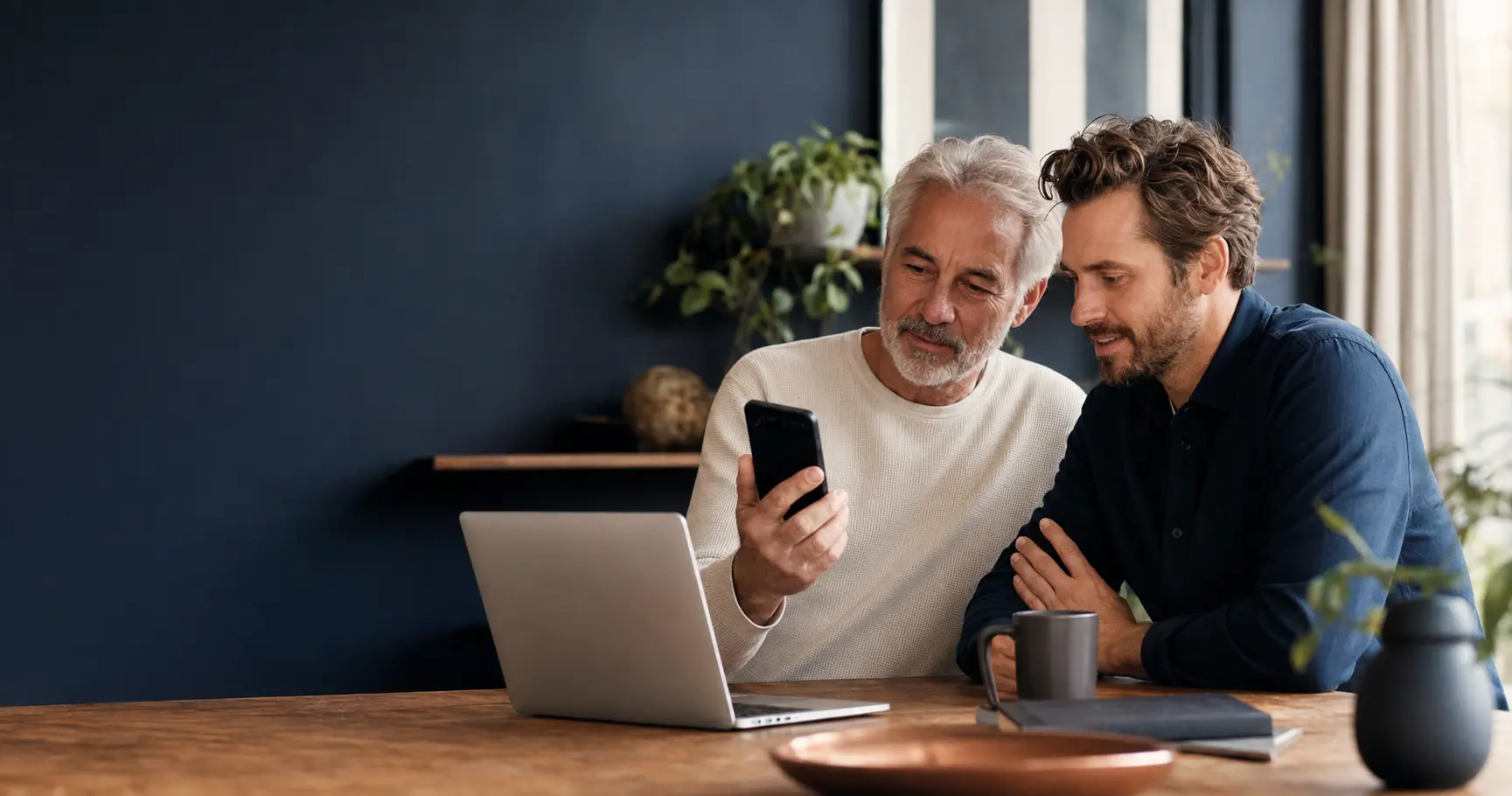 Zwei Erwachsene verschiedener Generationen nutzen gemeinsam Smartphone und Laptop.